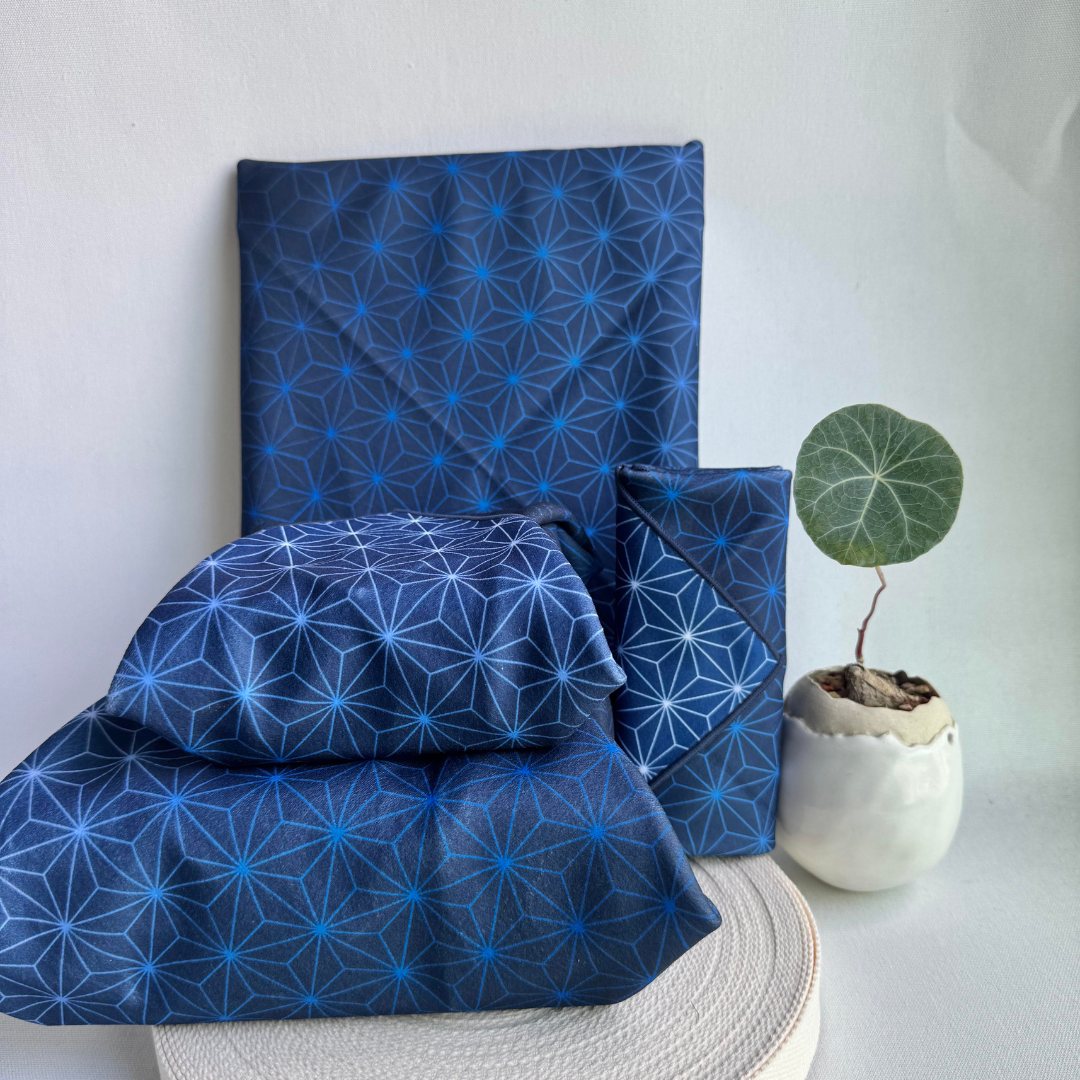 Blue Asanoha geometric patterned fabric wraps of different sizes on a white surface with a plant in the background