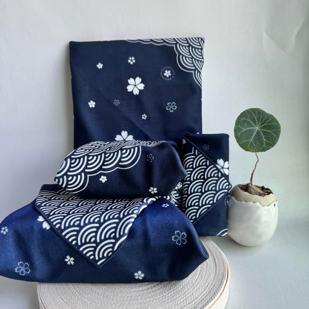 Blue fabric wraps with white sakura and seigaiha (wave) pattern of different sizes on a white surface with a plant in the background