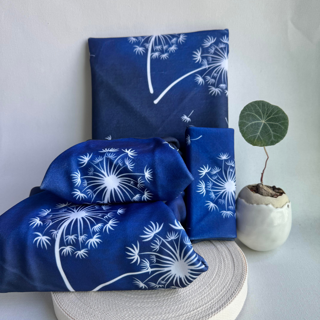 Blue fabric wraps with dandelion pattern of different sizes on a white surface with a plant in the background