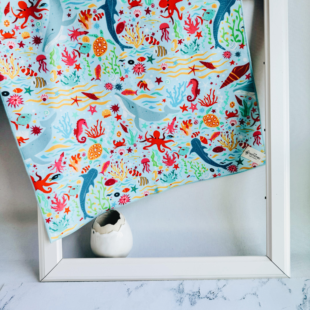 Tsutsumi Clingy Wrap with marine creatures artwork on light blue background, draped over a picture frame.