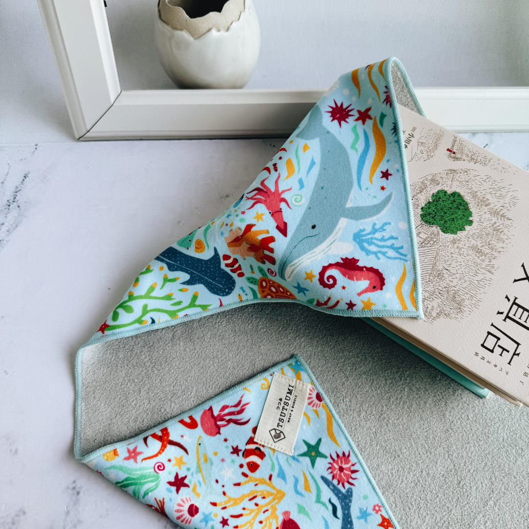 Half opened Tsutsumi Clingy Wrap with marine creatures artwork on light blue background, used to wrap some books.