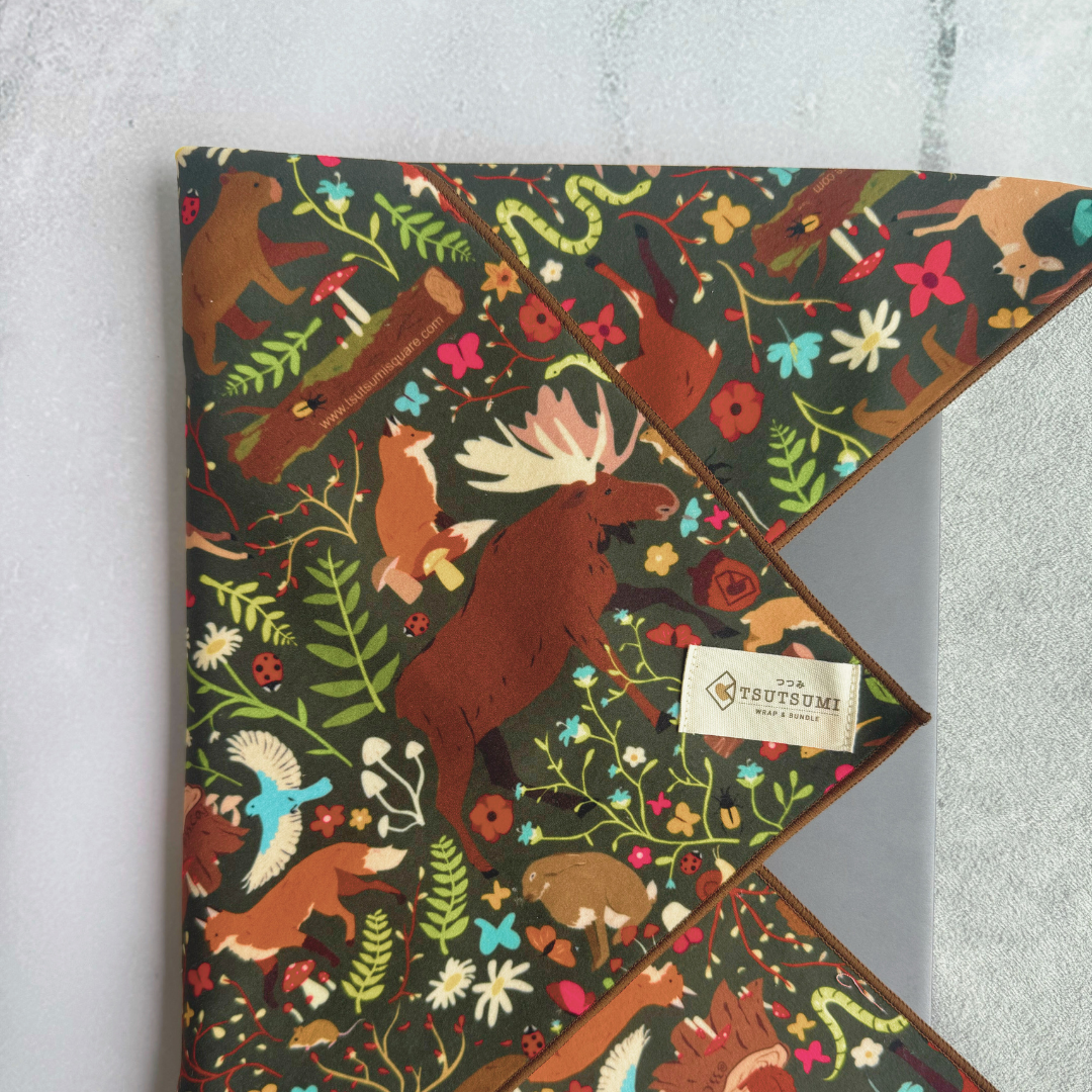 Tsutsumi Clingy Wrap with woodland creatures artwork and dark green background used to wrap a laptop.