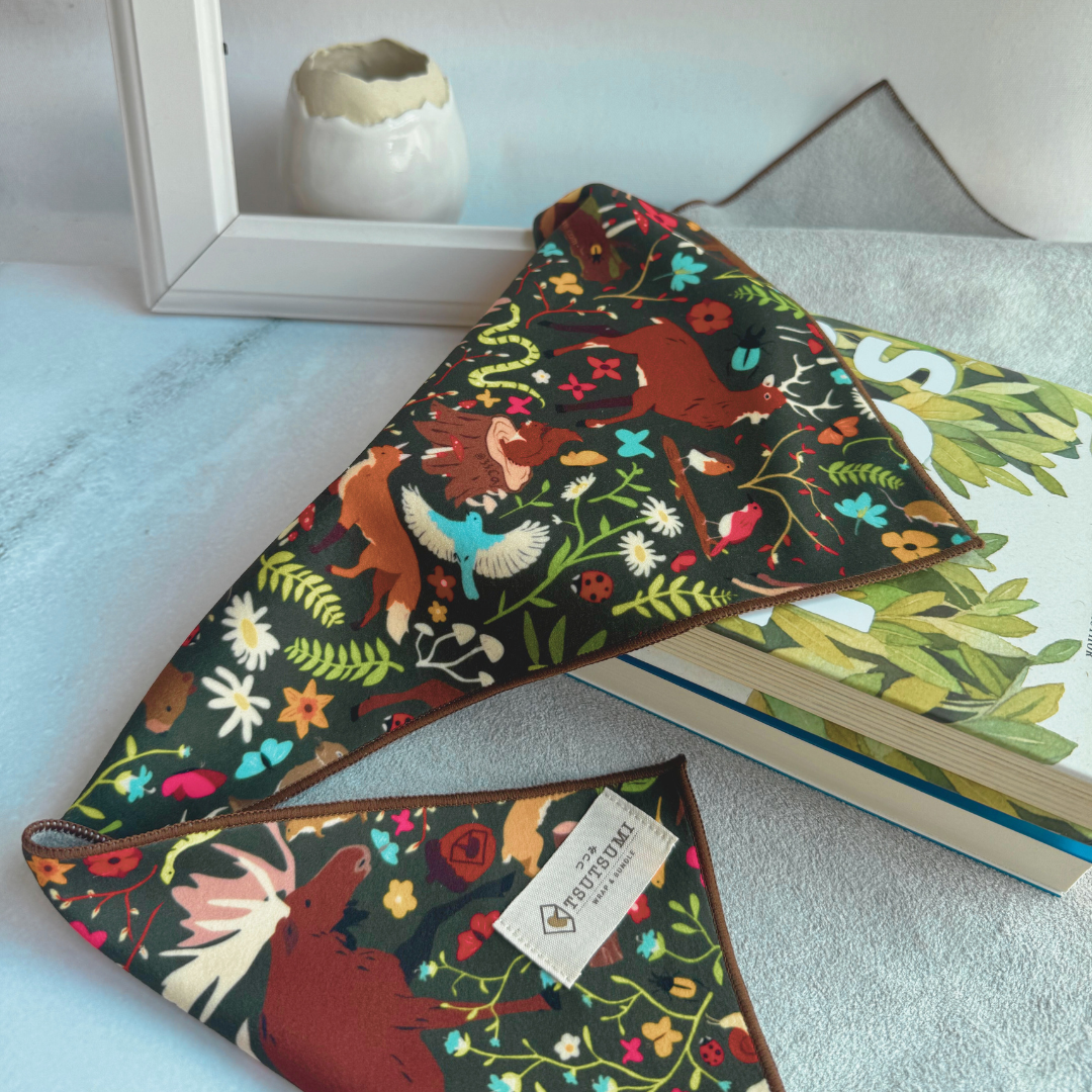 Half opened Tsutsumi Clingy Wrap with woodland creatures artwork with dark green background, used to wrap some books.