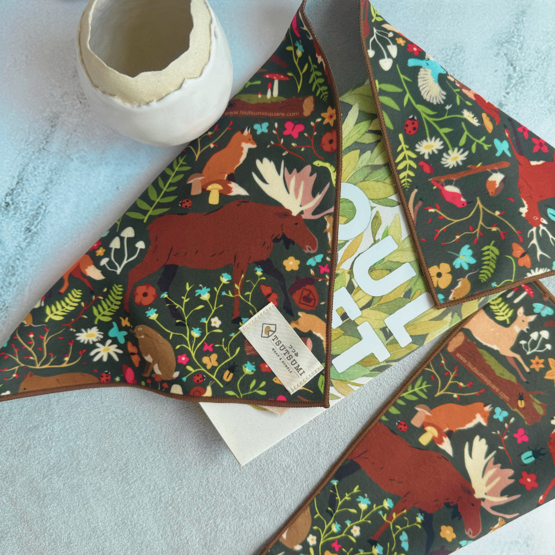 Half opened Tsutsumi Clingy Wrap with woodland creatures artwork and dark green background used to wrap some books.