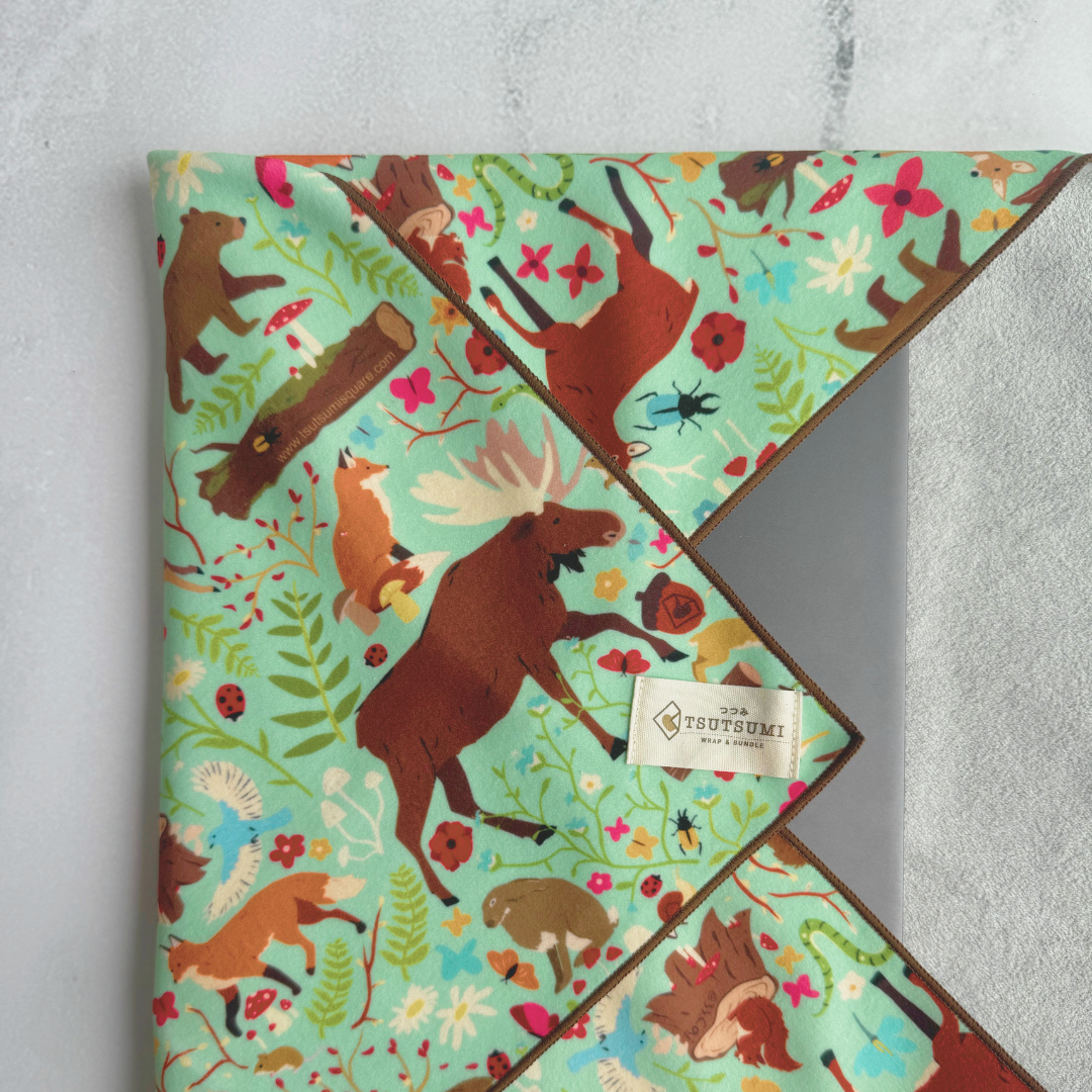 Tsutsumi Clingy Wrap with woodland creatures artwork on mint green background, used to wrap a laptop.