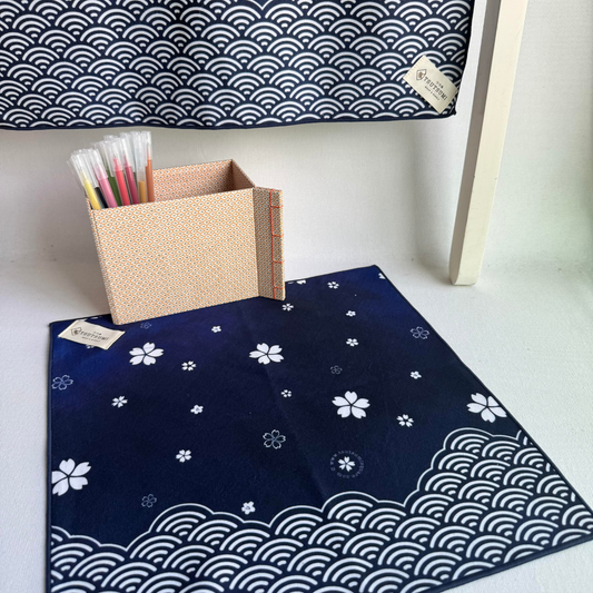 Two blue fabric squares with white sakura and seigaiha (wave) design, with a box of colorful pens