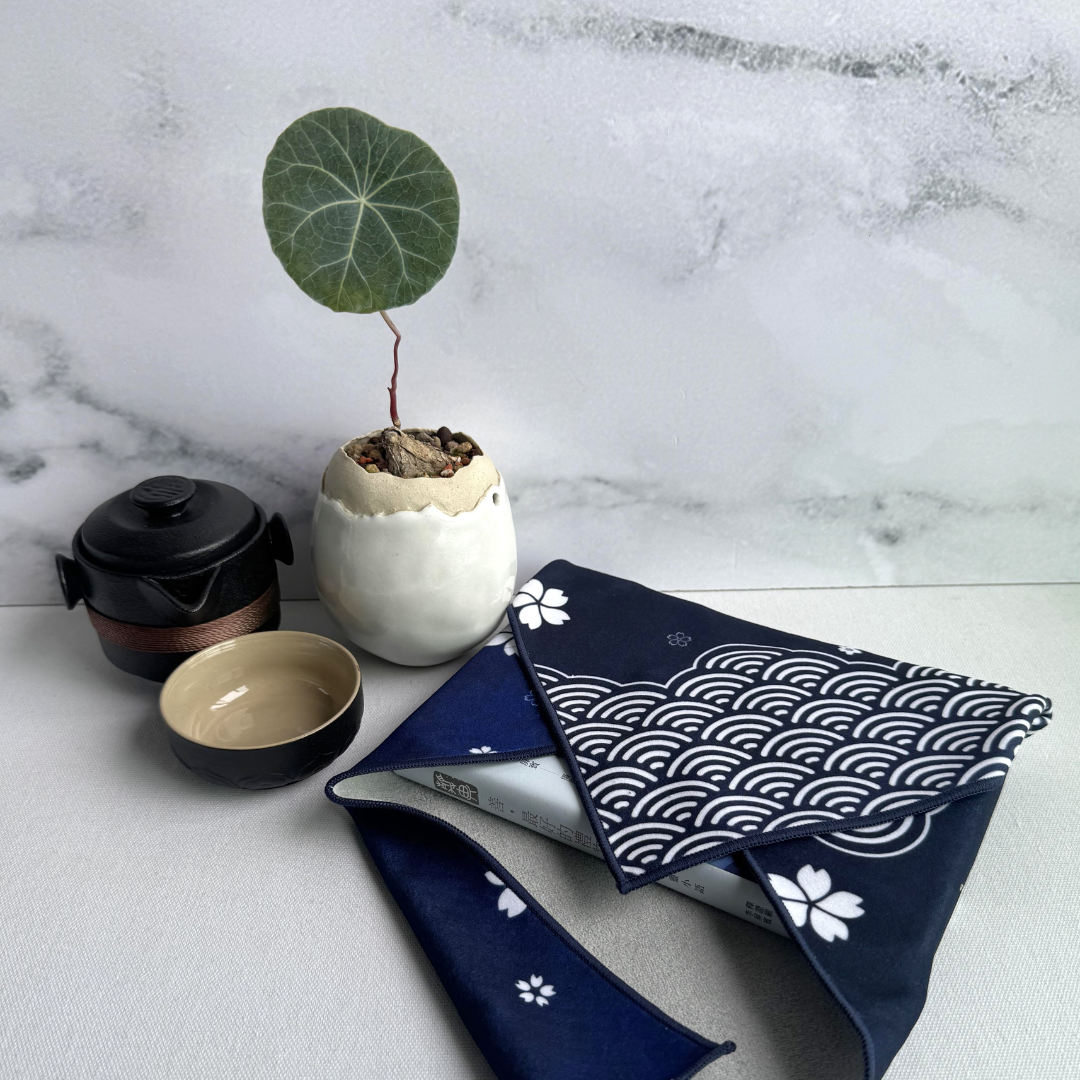 Blue fabric wrap with white sakura and seigaiha (wave) pattern on a marble surface with a small plant and teapot