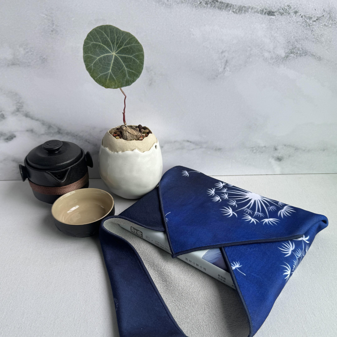 Blue patterned fabric with dandelion pattern wrap on a marble surface with a small plant and teapot.