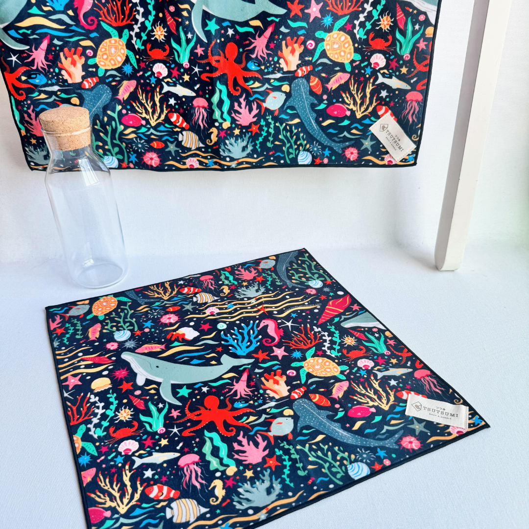 A big fabric in Marine Fantasy print in dark blue background hanging from a rack and a small piece of fabric with Marine Fantasy print in dark blue background laying on the table.