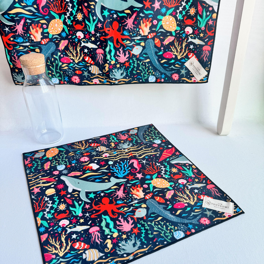 A big fabric in Marine Fantasy print in dark blue background hanging from a rack and a small piece of fabric with Marine Fantasy print in dark blue background laying on the table.