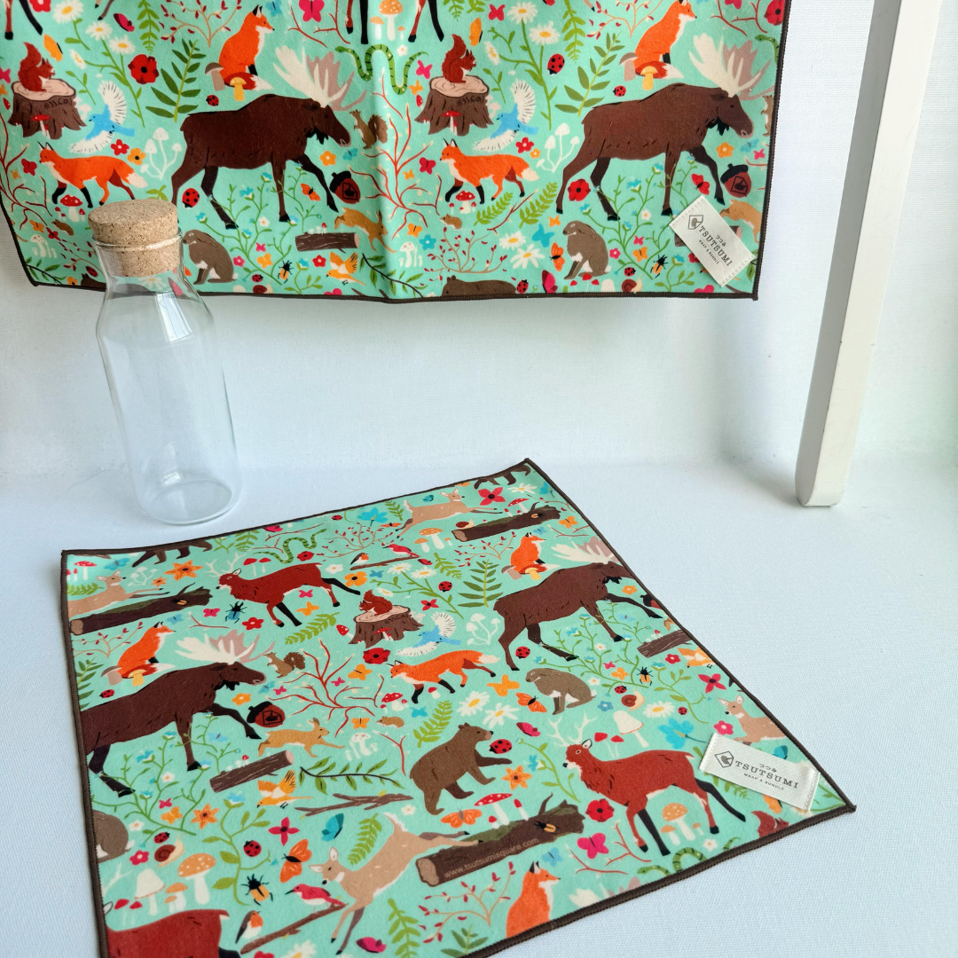 Fantasy print in mint green background hanging from a rack and a small piece of fabric with Woodland Fantasy print in mint green background laying on the table