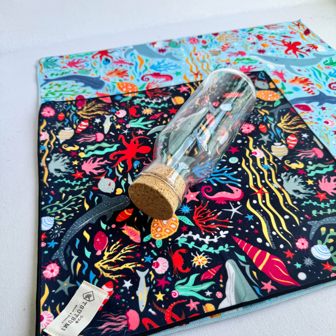 A small clingy wrap sitting on top of a bigger clingy wrap, and a glass bottle lying on top of both.