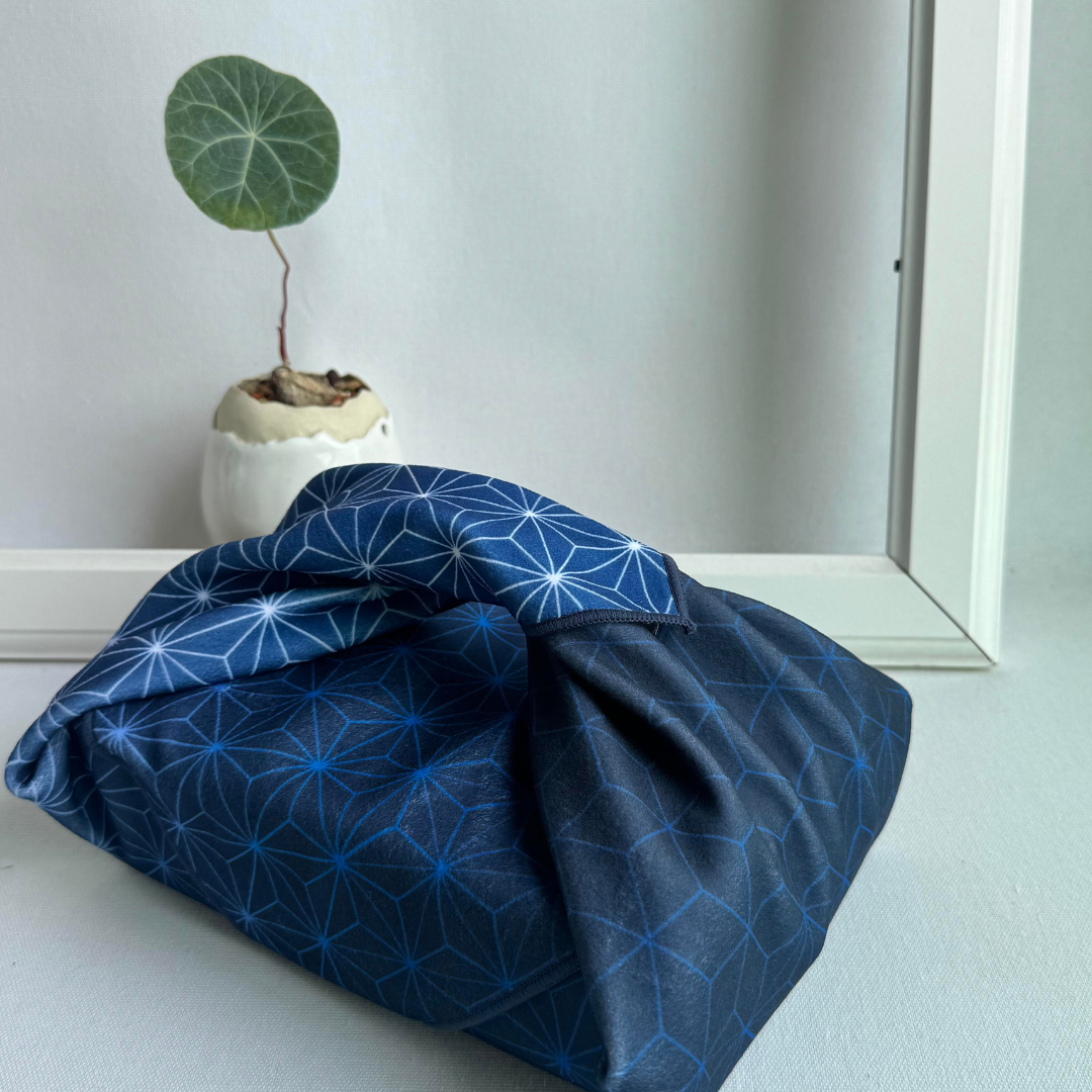 Blue fabric with Asanoha geometric pattern wrapping a lunchbox, next to a small potted plant.