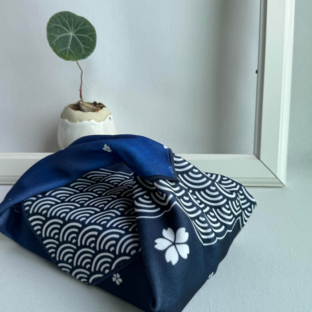 Blue fabric with sakura and seigaiha pattern wrapping a lunchbox, next to a small potted plant.