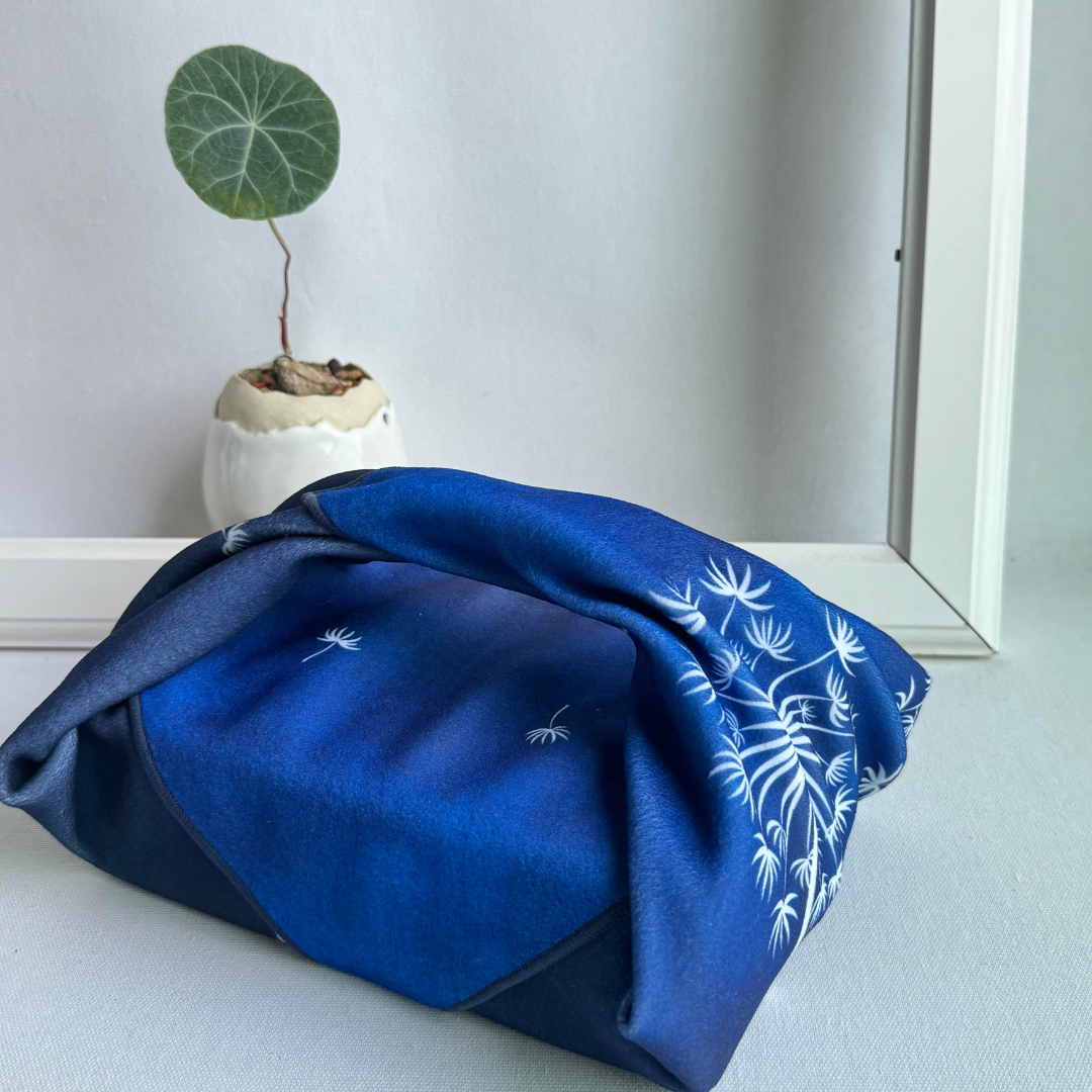 Blue fabric with Tanpopo (dandelion) pattern wrapping a lunchbox, next to a small potted plant.