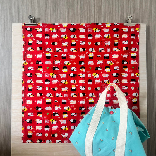 Fabric with Cats and Sushi icons and red background, and Tsutsumi square wrap used for wrapping a lunchbox