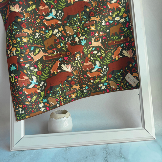 Tsutsumi Clingy Wrap with woodland creatures artworkt and dark green background draped over a picture frame.