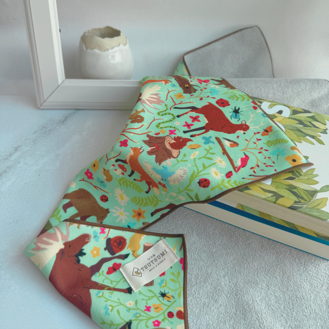 Half opened Tsutsumi Clingy Wrap with woodland creatures artwork on mint green background, used to wrap some books.