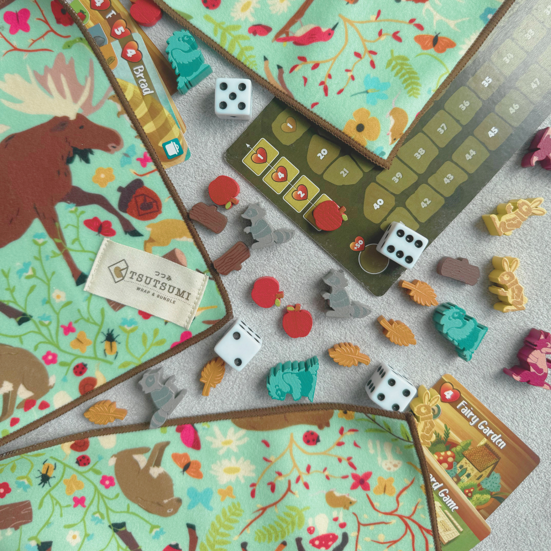 Half opened Tsutsumi Clingy Wrap with woodland creatures artwork on mint green background, used to wrap some board game tokens, dies and cards.
