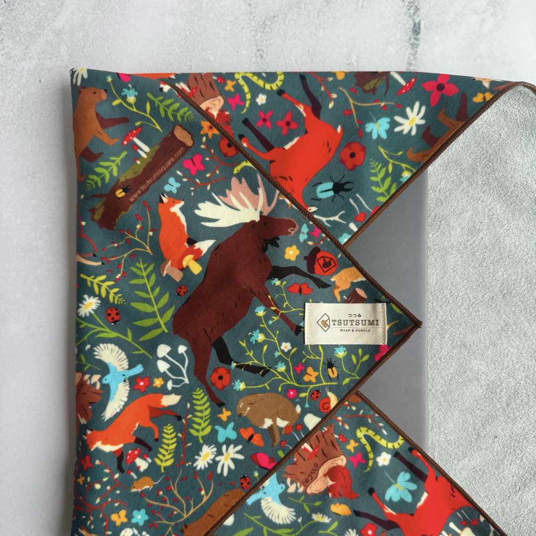 Tsutsumi Clingy Wrap with woodland creatures artwork on dark teal background, used to wrap a laptop.