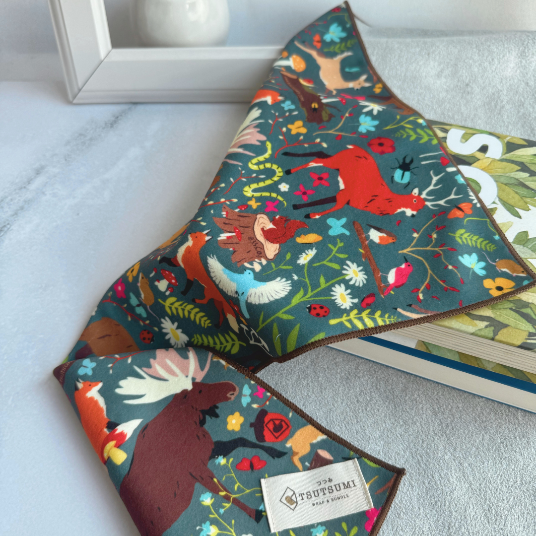 Half opened Tsutsumi Clingy Wrap with woodland creatures artwork on dark teal background, used to wrap some books.