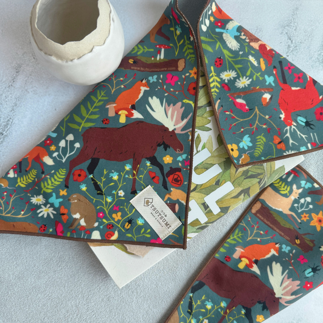 Half opened Tsutsumi Clingy Wrap with woodland creatures artwork on dark teal background, used to wrap some books.