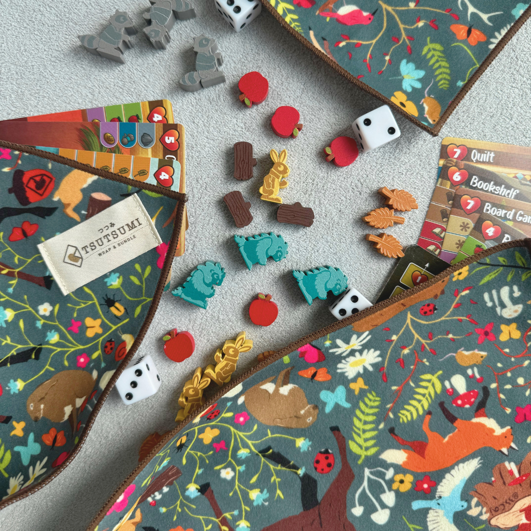 Half opened Tsutsumi Clingy Wrap with woodland creatures artwork on mint green some board game tokens, dies and cards.