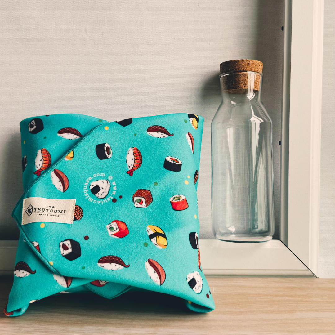 Blue fabric with sushi pattern wrapping some books next to a glass bottle on a wooden surface.