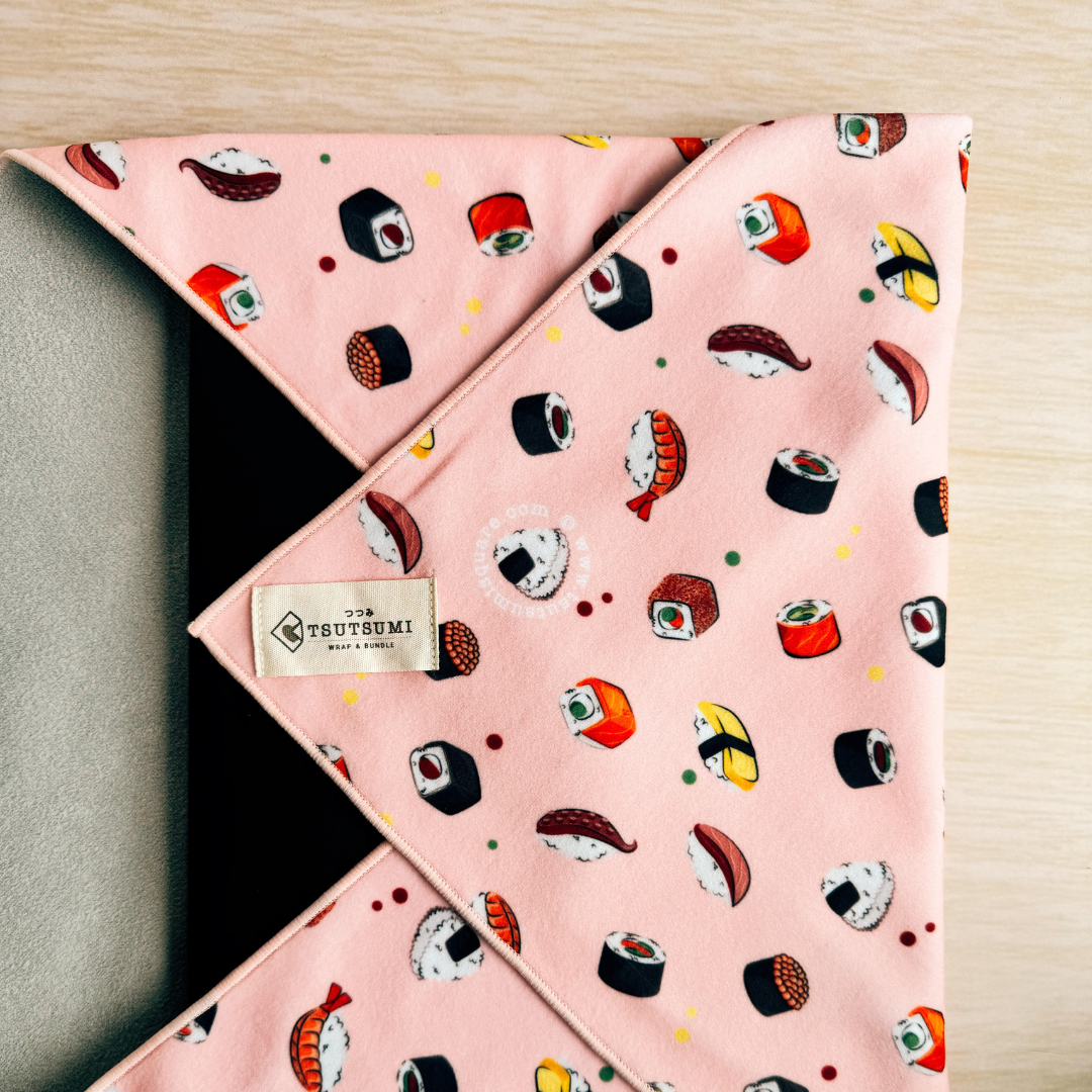 Pink fabric with sushi pattern and 'TSUTSUMI' label wrapping a laptop