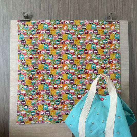 Fabric with cute and colourful Daruma figures, and a Tsutsumi square wrap in use