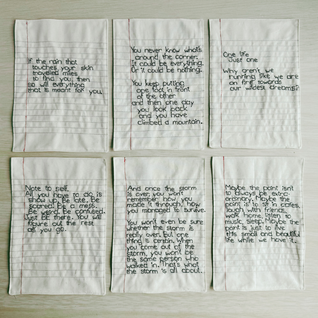 Six pieces of lined fabric with handstitched text on a wooden surface