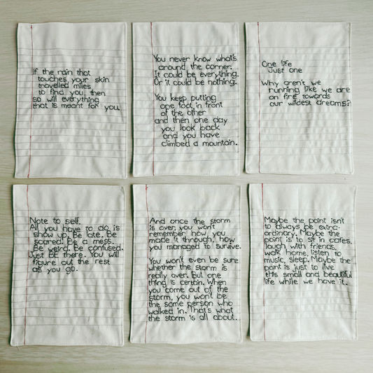 Six pieces of lined fabric with handstitched text on a wooden surface