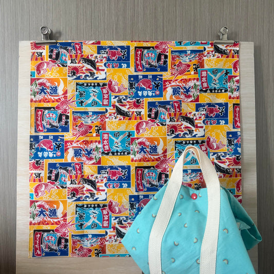 Fabric with Japanese Seafood icons and yellow background, and Tsutsumi square wrap used for wrapping a lunchbox