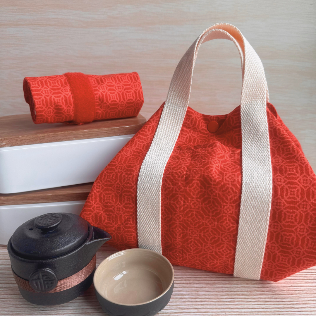 Red patterned bag with white straps, black teapot, and beige bowl on a wooden surface.
