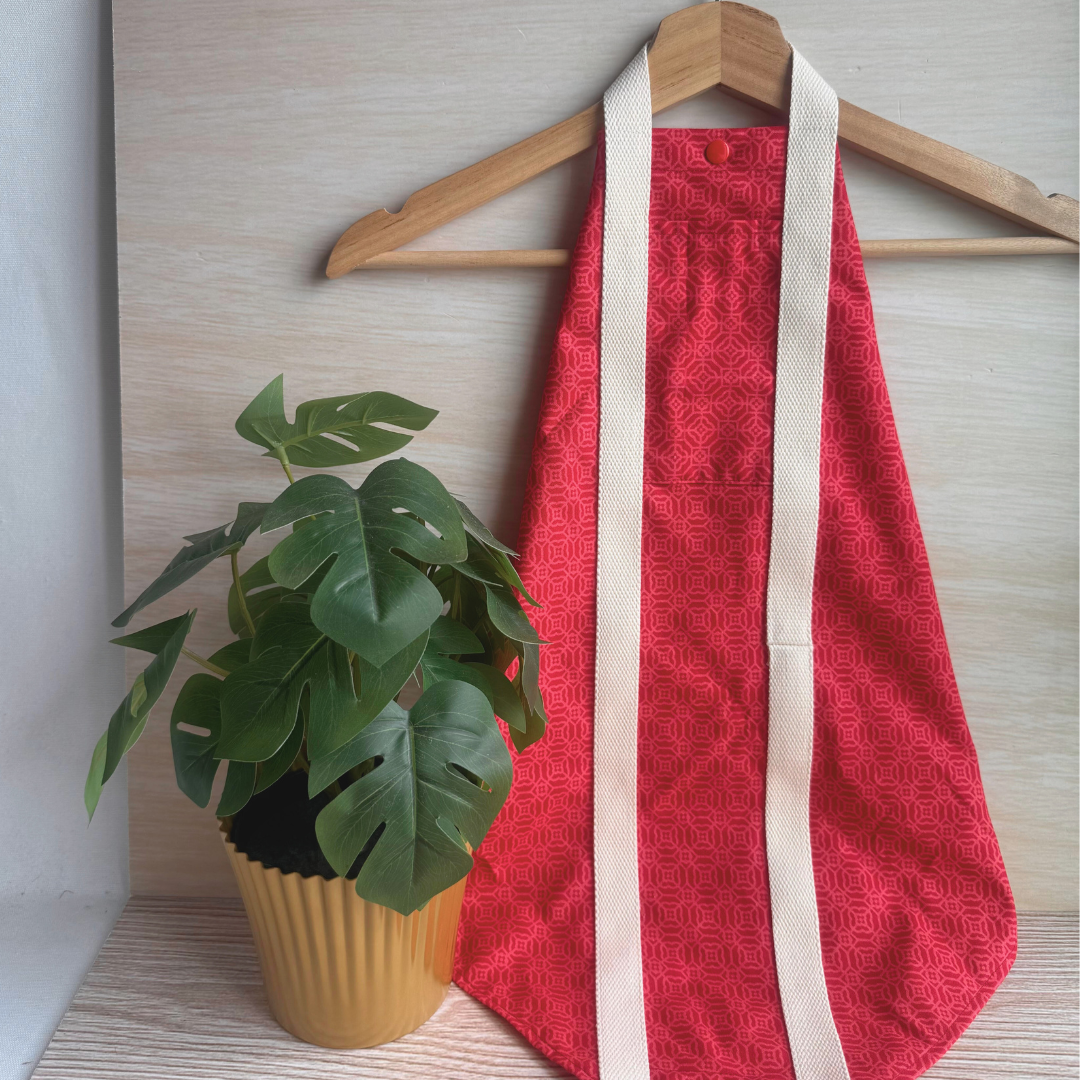Red textured fabric carrier with white straps on a wooden hanger next to a potted plant.