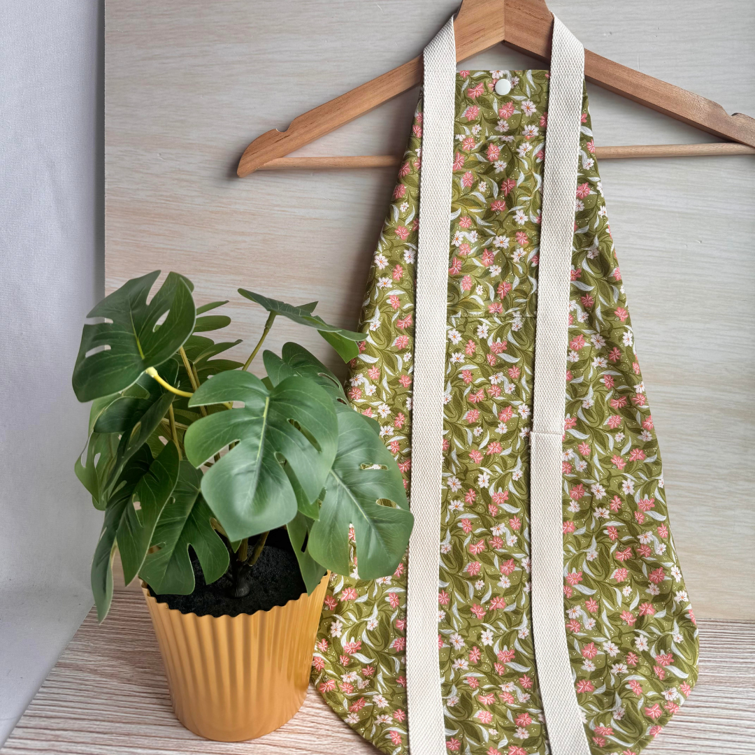 Floral-patterned fabric square wrap hanging from a hanger with a plant on a wooden surface