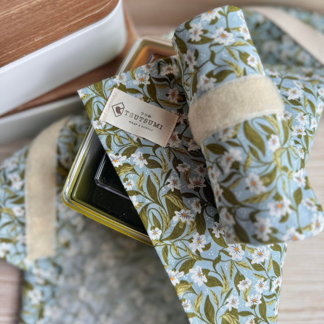 Floral-patterned fabric square wrap with a visible brand label half covering a plastic container.