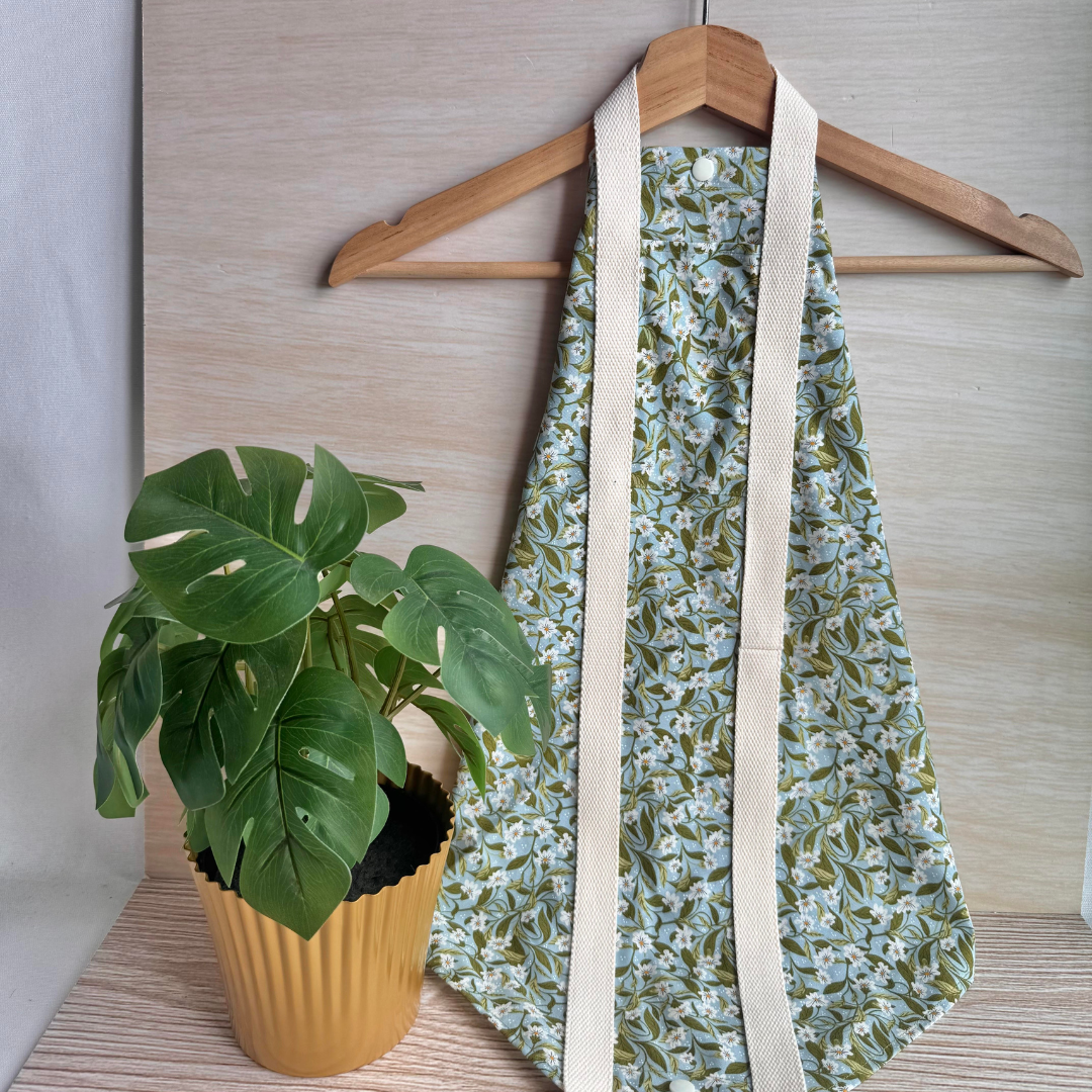 Floral-patterned fabric square wrap hanging on a hanger next to a potted plant on a wooden surface.