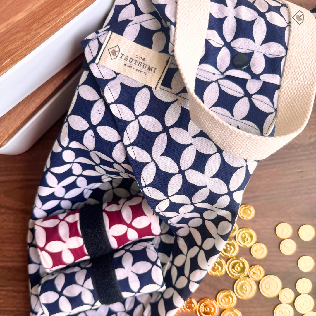 Navy and white geometric pattern on fabric with 'Tsutsumi' label on a wooden surface with coins.