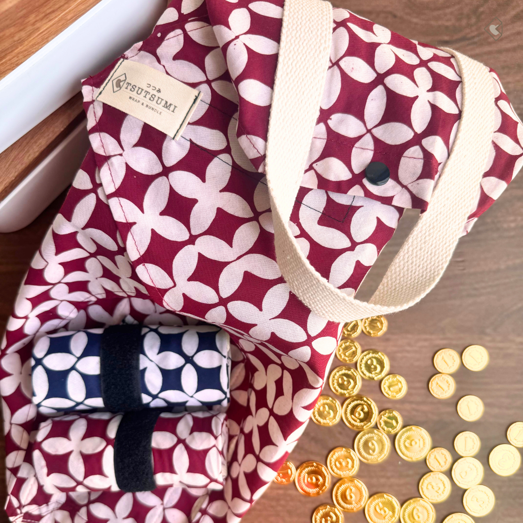 Red and white geometric pattern on fabric with 'Tsutsumi' label on a wooden surface with coins.