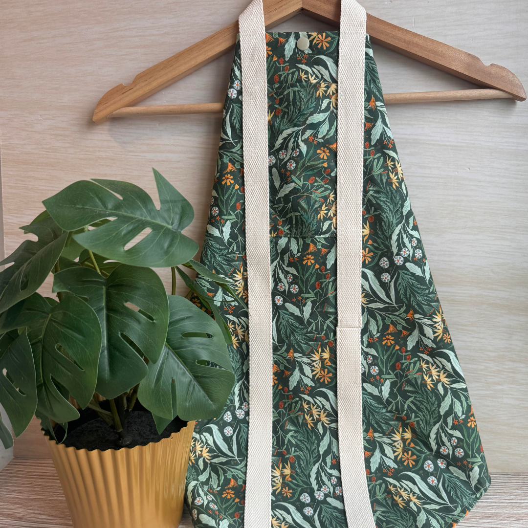 Green floral-patterned square wrap on a wooden hanger next to a potted plant.