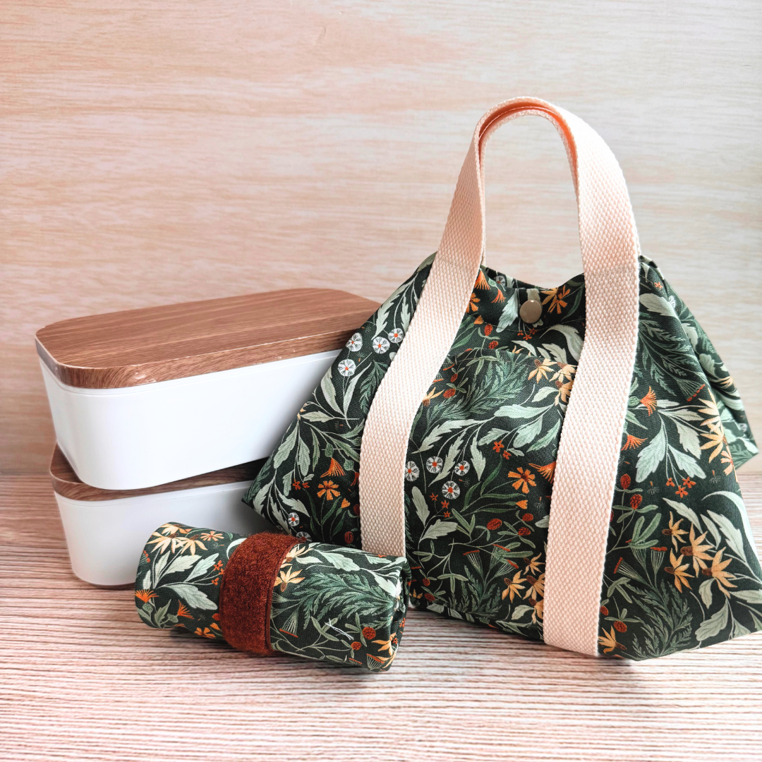 Fabric square wrap with green floral print and dark brown handles that looks like a bag for lunchboxes