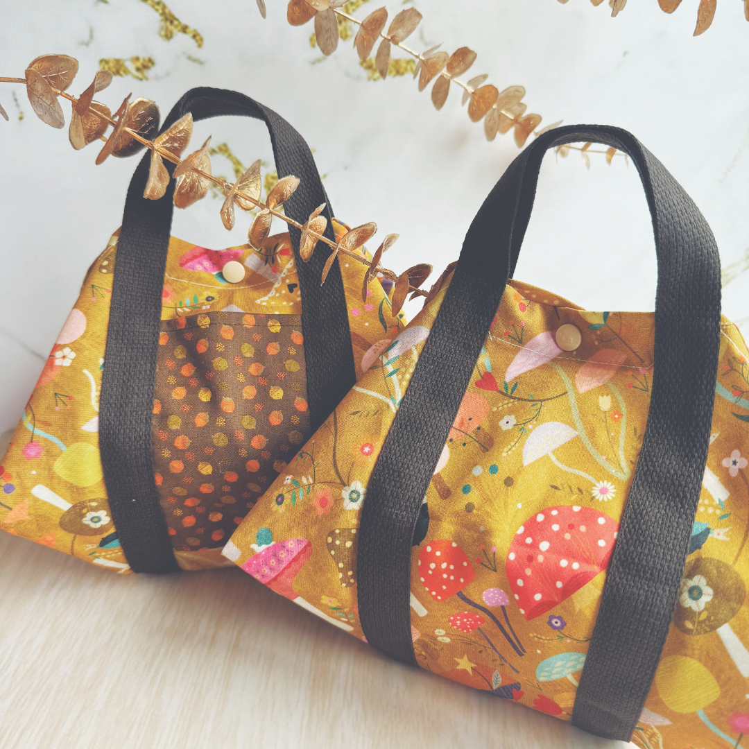 Two square cotton wraps with a floral and mushroom design, featuring black handles and straps on a marble background.